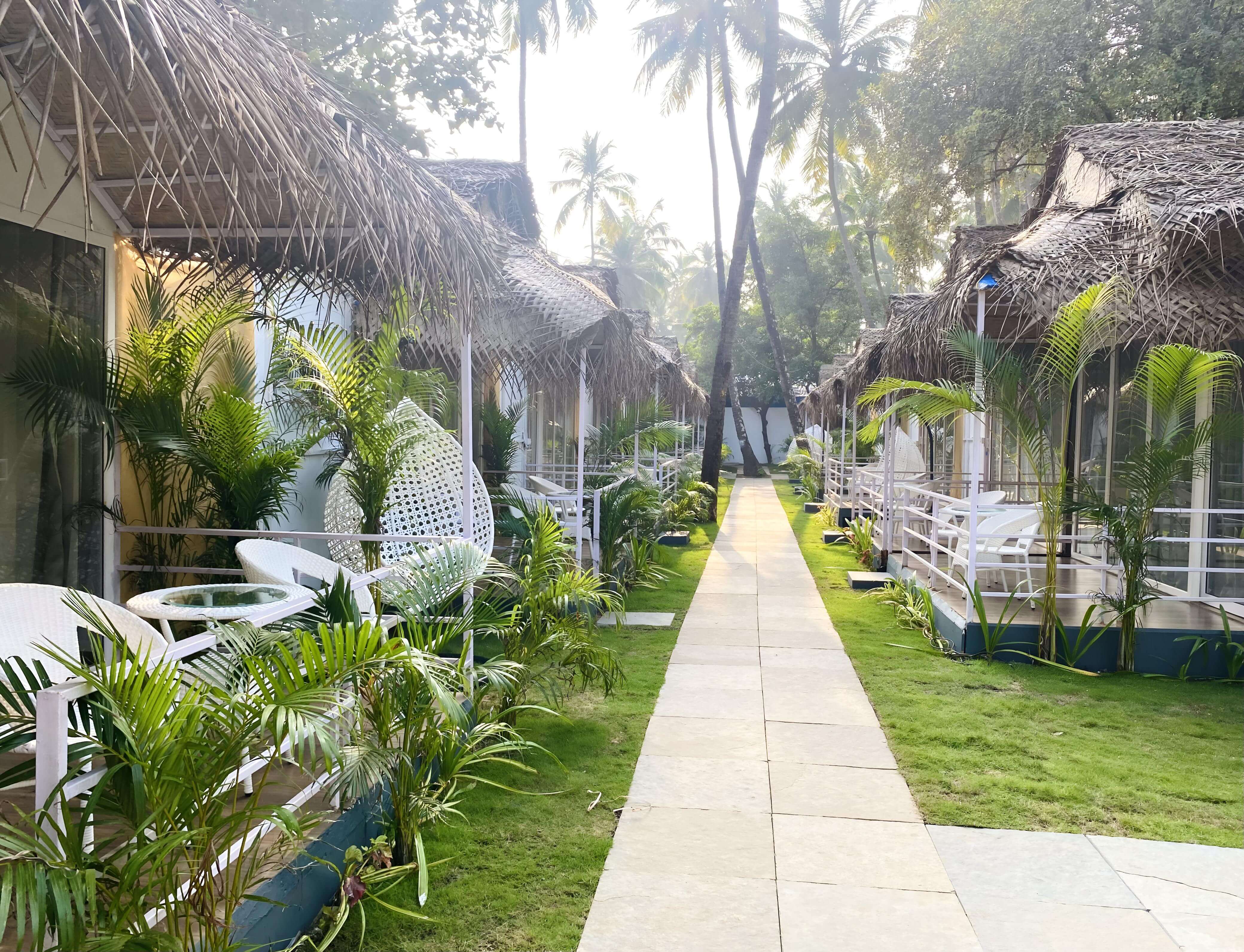 A tranquil walkway invites guests to a beach resort, showcasing beautiful thatched-roof cottages.